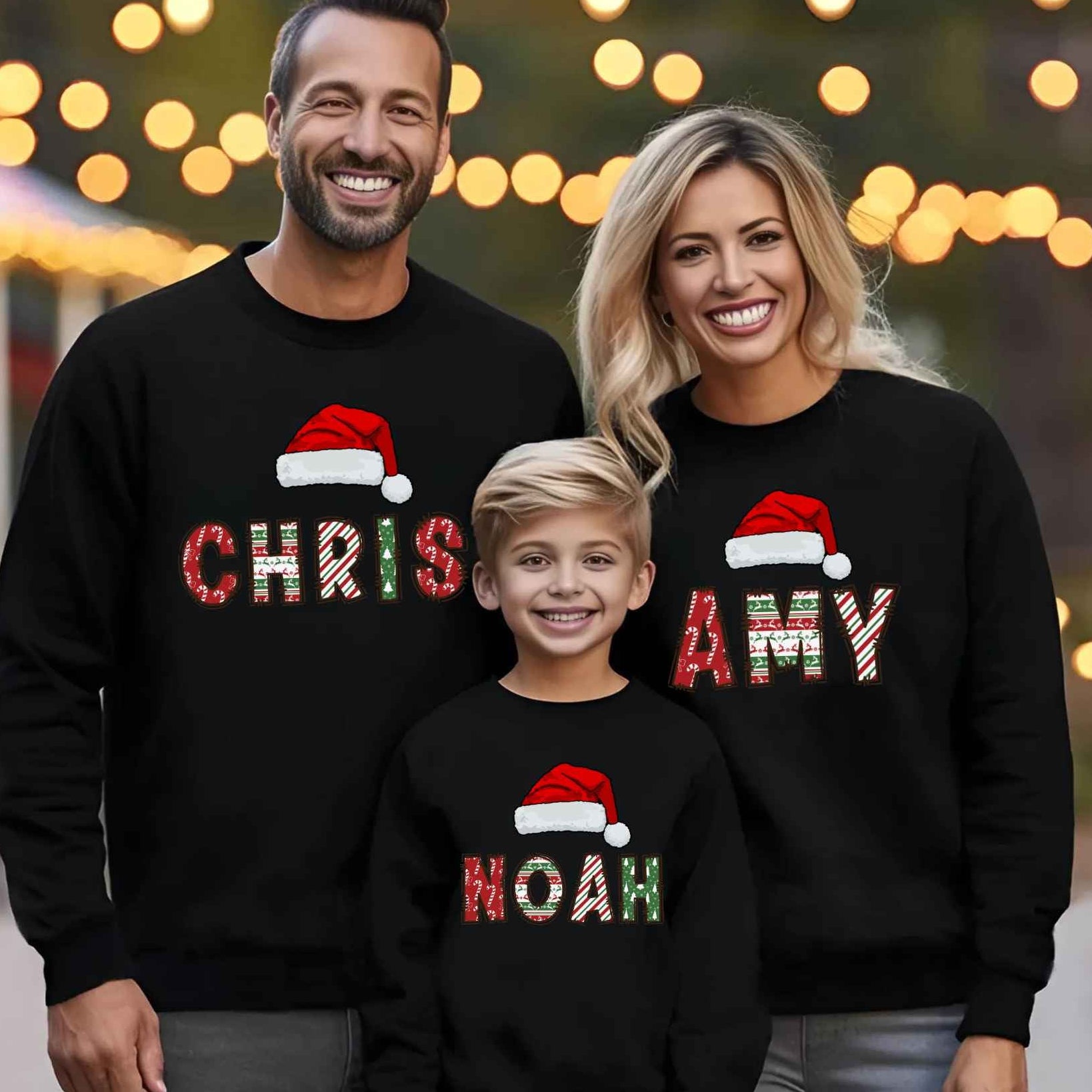 Family of three wearing matching black Christmas-themed sweatshirts with names and Santa hats.